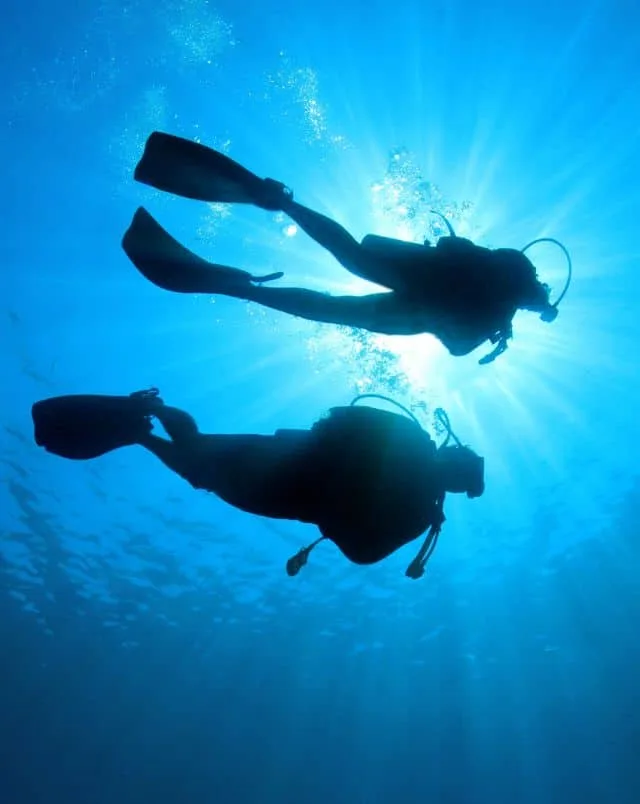 Best outdoor activities in Carvoeiro, Upwards underwater view of the silhouettes of two people in scuba diving gear swimming past slowly overhead with the light from the sun behind them