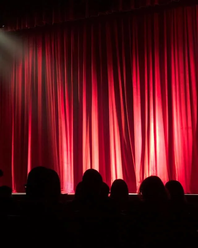 Best things to do on Halloween in MilwaukeeView of red curtain on stage from behind a few rows of heads in the dark