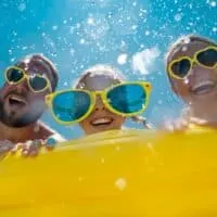 Ultimate guide to water parks in Tenerife, Smiling family all wearing heart-shaped sunglasses sitting on inflatable raft while water sprays around them in the sun