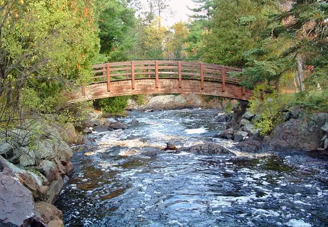 spring break destinations in Wisconsin, wooden bridge over rocky river surrounded by trees