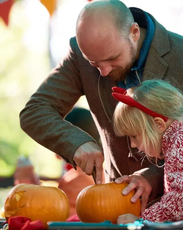 Fun events in Wisconsin in October, Man cutting into a pumpkin during a pumpkin carving event while a young girl watches closely