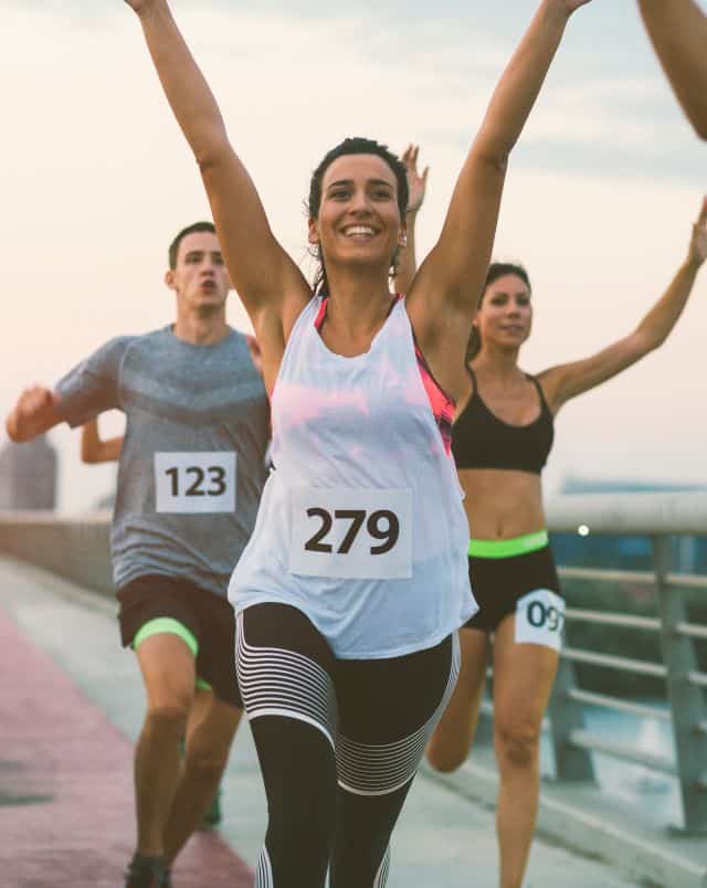 Door County fall activities, Several people in marathon sportswear running across a bridge as the sun sets towards a finish line with their arms raised and smiling