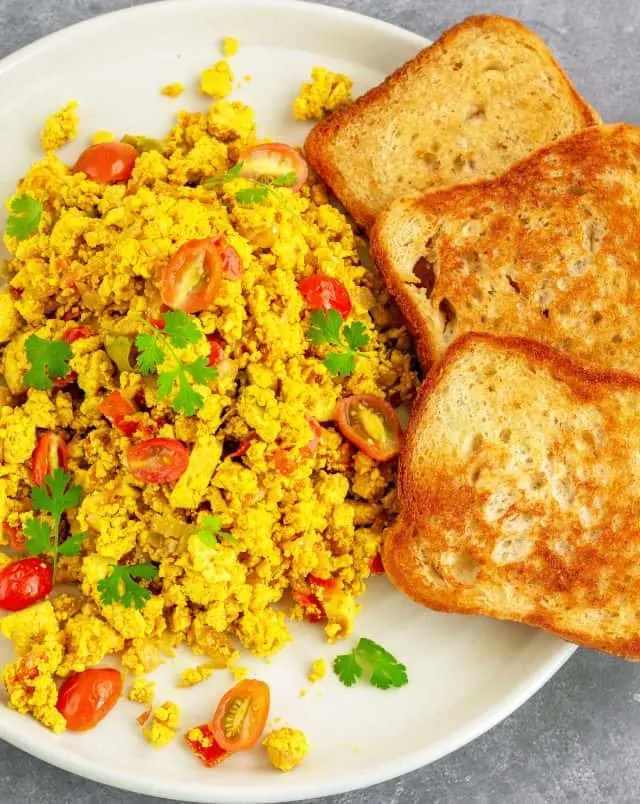 vegan brunch in Milwaukee, Overhead shot of a plate of vibrant yellow tofu scramble with chopped cherry tomatoes and green herb seasoning with three slices of fried bread on the side
