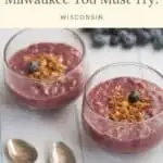 Pin with image of two wide glasses containing fruity yogurt topped with diced nuts and a single blueberry with a pile of blueberries behind and two silver spoons in front, caption reads: Vegan Restaurants in Milwaukee You Must Try! Wisconsin from Paulina On The Road