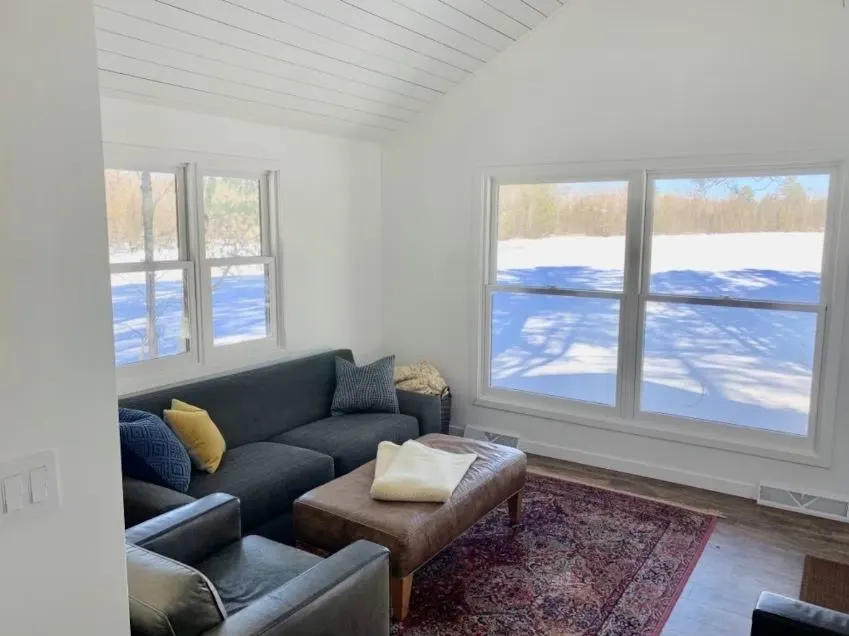 living room with a sofa and big windows overlooking the yard in winter at the Nordic Cabin - Seeley, Wisconsin