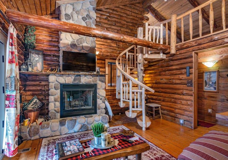 wooden living room with fire place and staircase at the Log Cabin in 10 Acre Forest in Wisconsin Dells - 12 Fun Dog-Friendly Cabins in Wisconsin Dells