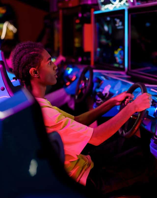 Fun fall activities in Milwaukee, Person sitting behind the wheel of a video arcade driving game whilst lit by fluorescent red and blue lights