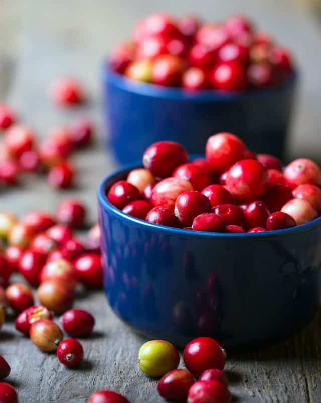 Cranberry fall festivals in Wisconsin, Two small blue bowls full of cranberries on wooden table surrounded by more loose cranberries