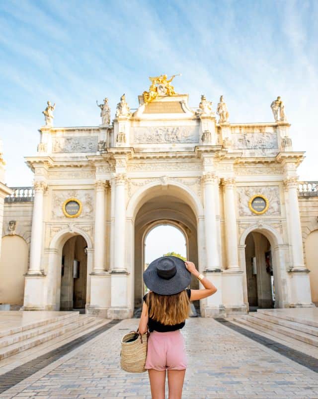 Try out some of the best day tours from Luxembourg City, person in sunhat looking up at a large ornate gateway at the edge of a wide stone-tiled courtyard