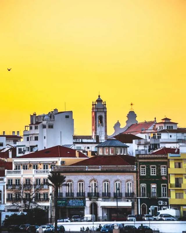 day trips in Portugal from Lagos, View of Portimão looking across the rooftops of many apartment buildings and churches clustered together under a blazing yellow sky at sunset