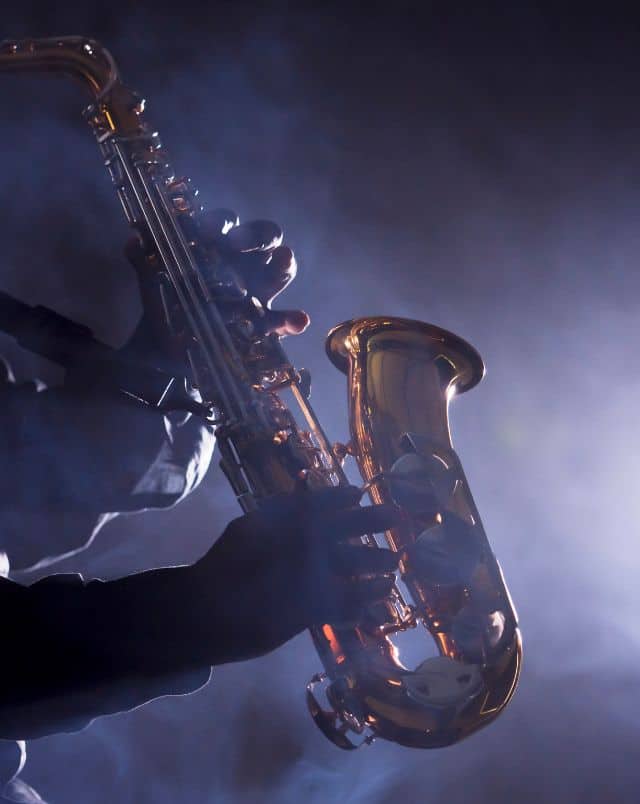 Enjoy Milwaukee at night, Close up of a person's hands holding an alto saxophone as they play it in a dark room surrounded by bright mist
