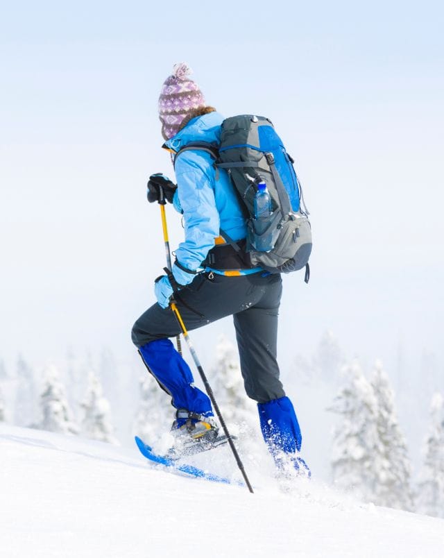 winter date ideas in Wisconsin, Person wearing outdoor clothing including a woolen hat and a backpack using skis and poles to walk up a hill blanketed in white snow
