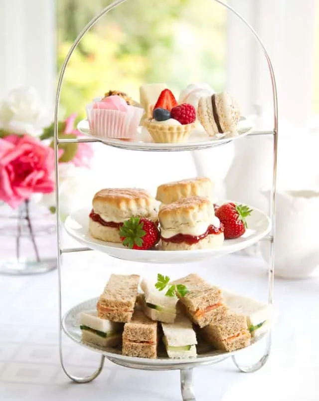 Enjoy Milwaukee in December, Close up shot of a tiered cake holder stacked with three plates ready for afternoon tea containing small sandwiches on the bottom level, scones with cream and jam on the middle level and cupcakes on the top level