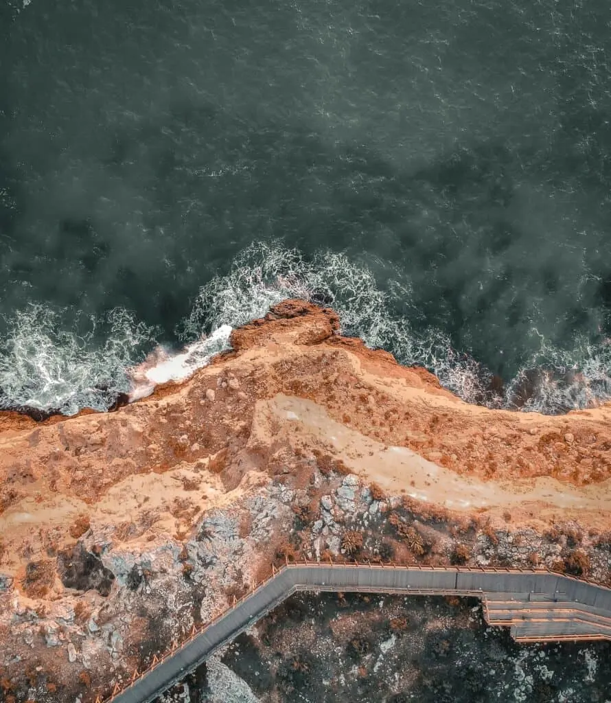 An aerial view of the ocean and a cliff with a wooden walkway.