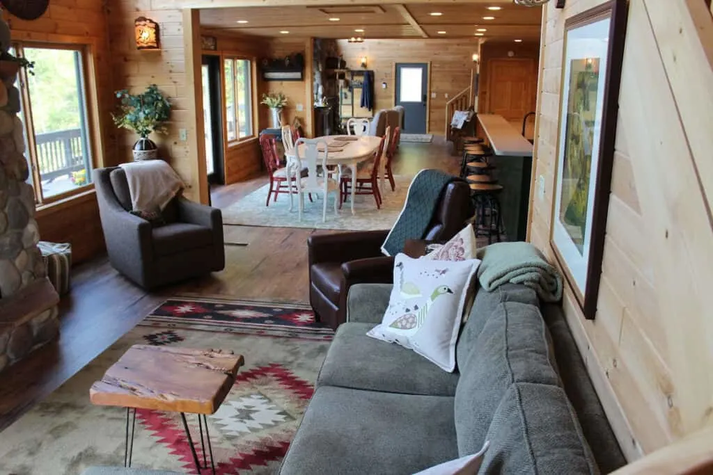 best luxury cabin rentals in wisconsin, Interior living room spaces with long comfortable couches and soft armchairs in one area and long dining table and chairs and a breakfast bar visible behind