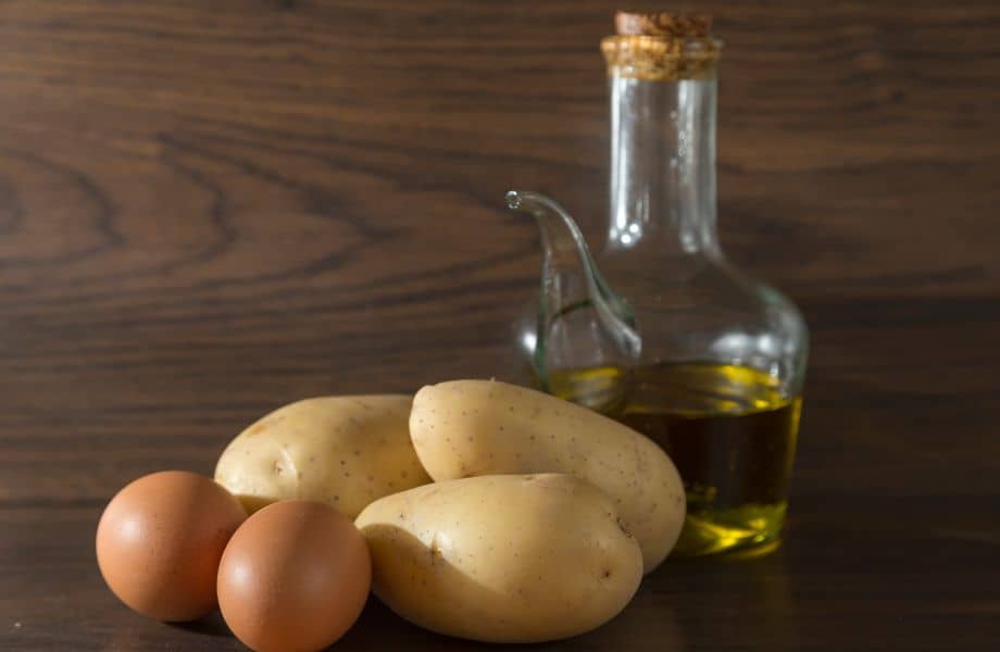what to eat in Algarve in December, Close up shot of a trio of potatoes and two eggs sitting next to a glass flask of olive oil with a thin spout and a large cork in the top