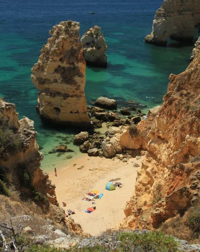 Fun holidays in Carvoeiro, View of people sunbathing on a golden sandy beach surrounded by tall rocky cliffs next to the clear turquoise waters of the sea