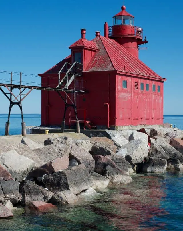 Door County activities in March, Small red painted lighthouse and accompanying red painted lighthouse keeper's house sitting on a rocky jetty in front of a calm sea under a clear blue sky