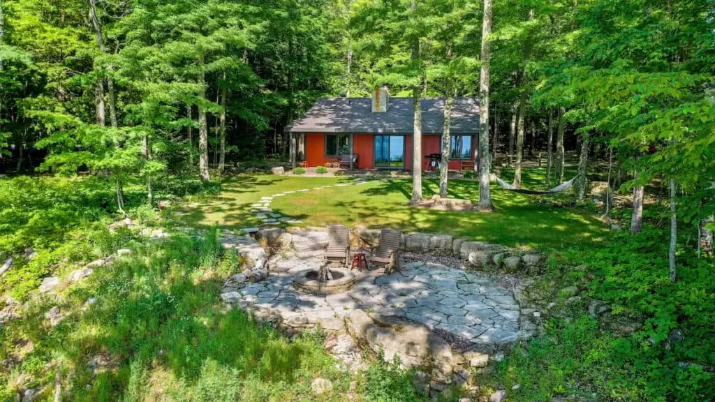 luxury cabin rentals in wisconsin, View of outdoor luxury cabin nestled amongst a forest of vibrant green trees with a fire pit and gathering area in the foreground
