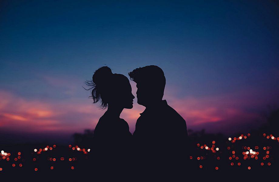 Most romantic things to do in Milwaukee Wisconsin, Silhouette of two people standing in front of the bright lights of a wide cityscape at dusk under a dark sky