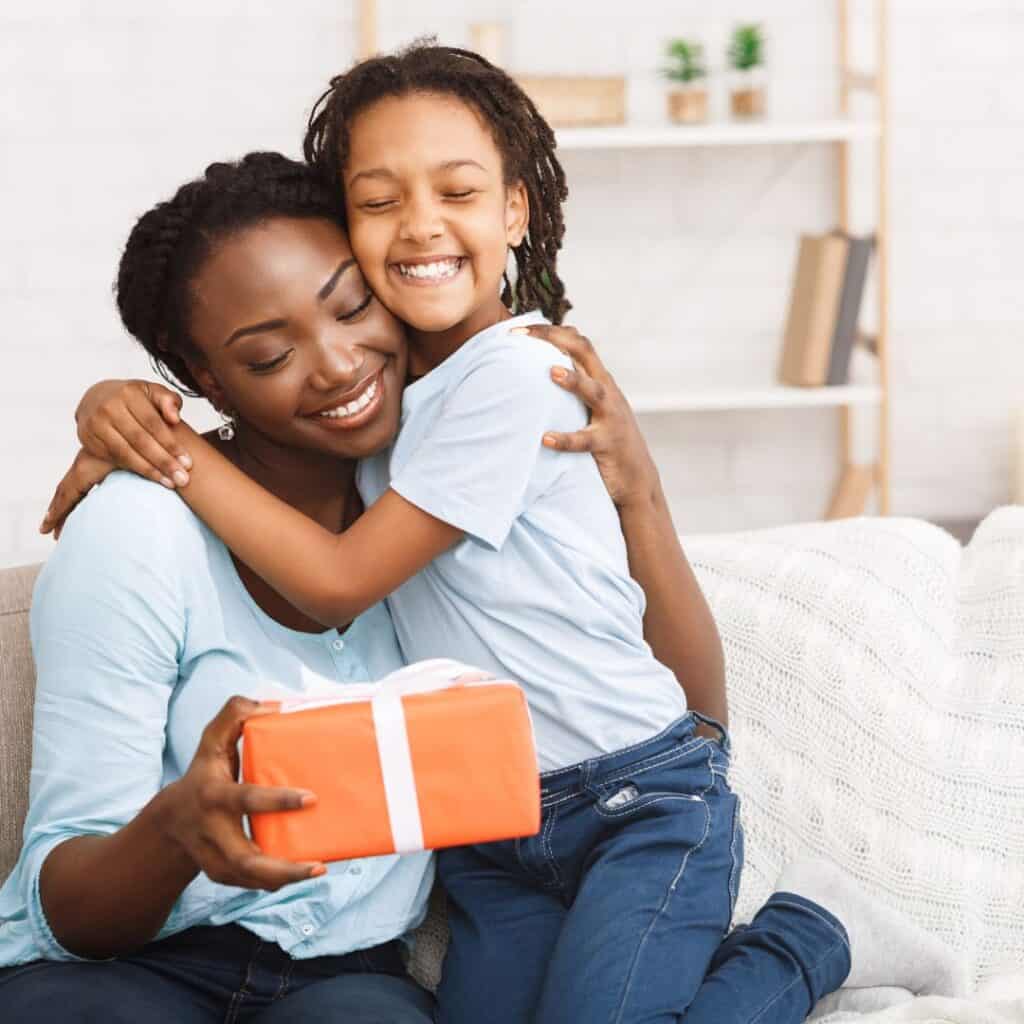 a girl hugging her mom who is holding an orange gift box from her daughter