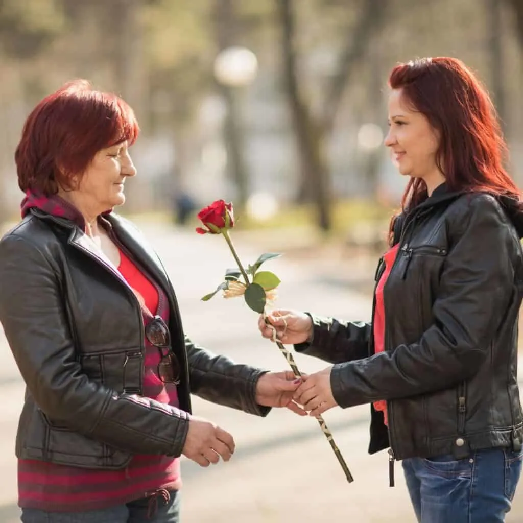 an older daughter giving a rose to her mom; both wearing red and leather jackers