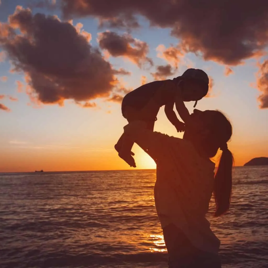 a silhouette of a mother raising her infant child during sunset
