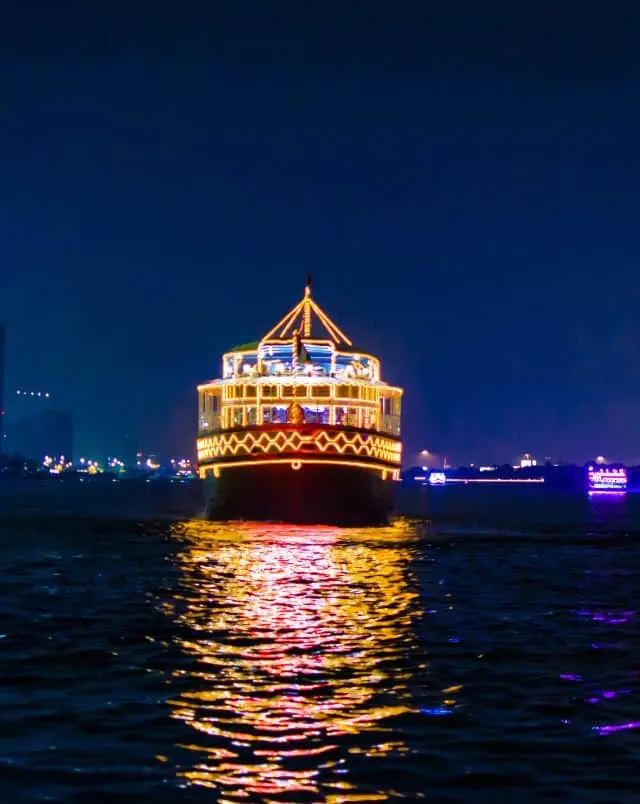 places to go on a date in Milwaukee, View of a large boat lit up with bright colorful lights as it sails down a wide river at nighttime