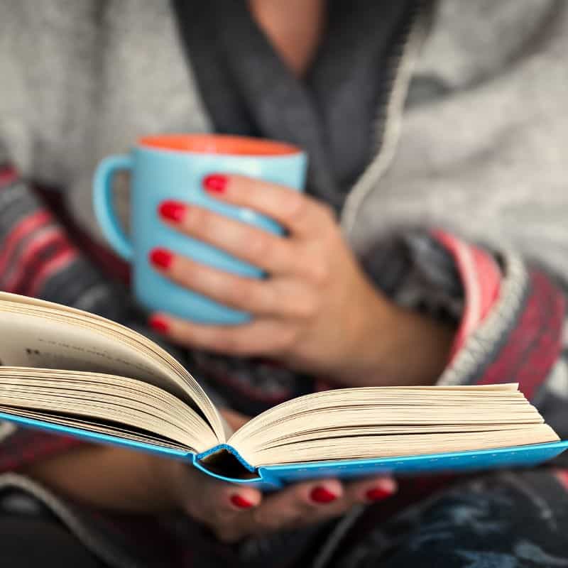 woman holding a cup of coffee and reading Coffee table books and adventure books