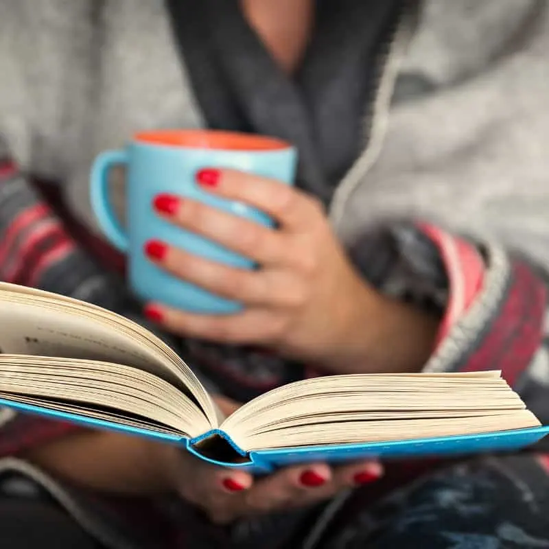 woman holding a cup of coffee and reading one of the best adventure books