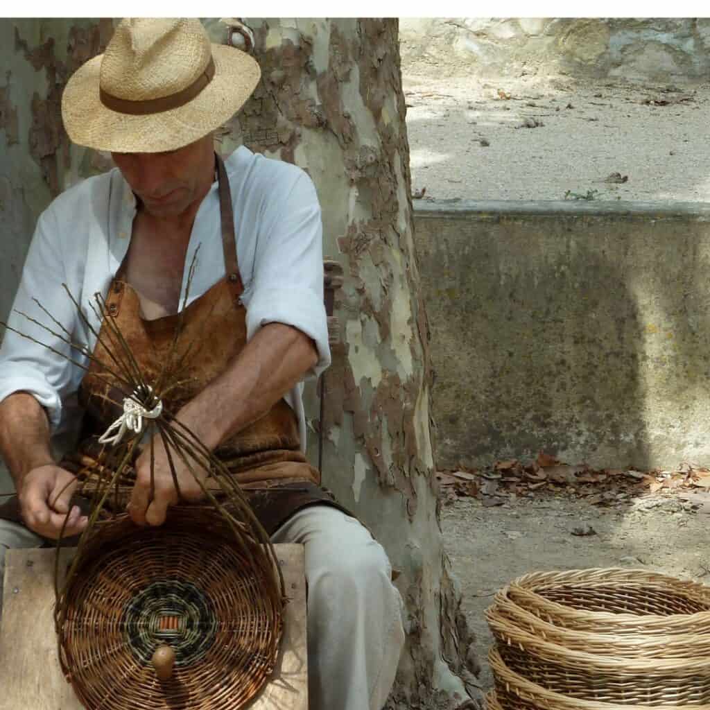 a man in a hat weaving a basket with other baskets finished on his side