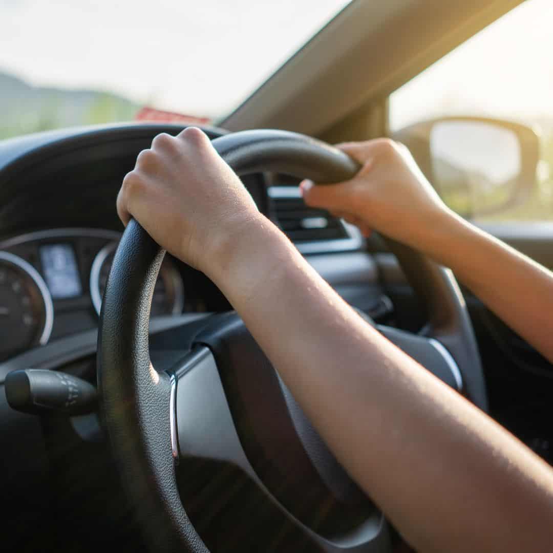 a closeup of a persons hands driving a car during the day