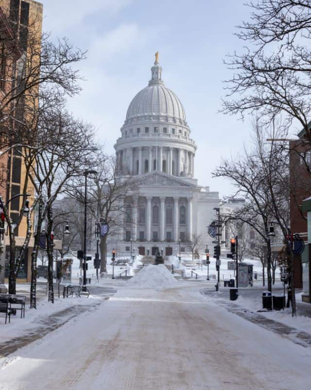 winter day trips from Milwaukee, View of Madison Capitol Building as seen at the end of a snow-covered street lined with bare winter trees under a bright cloudy sky