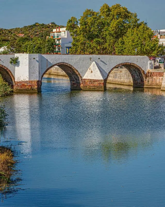 best things to see in Silves, View of roman bridge in Silves with neat brick arches standing over a river with buildings and green trees behind