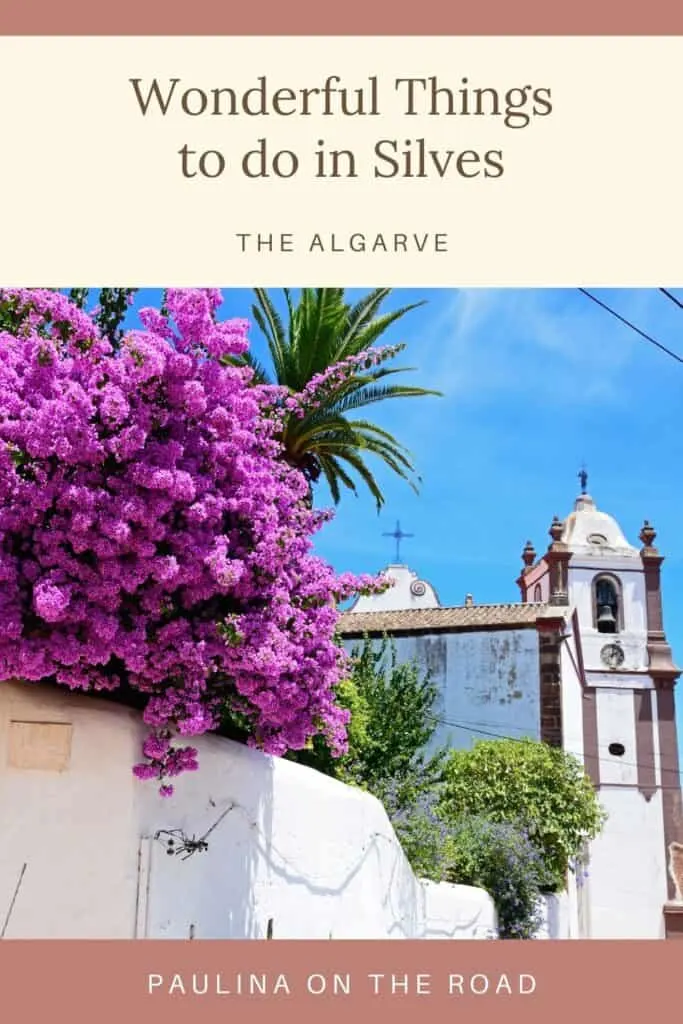 Pin with image of a white stone church with ornate embellishments and a bell tower and crucifixes on top with some vibrant purple and green flowers and shrubberies in the foreground, caption reads: Wonderful Things to do in Silves, The Algarve from Paulina on the Road