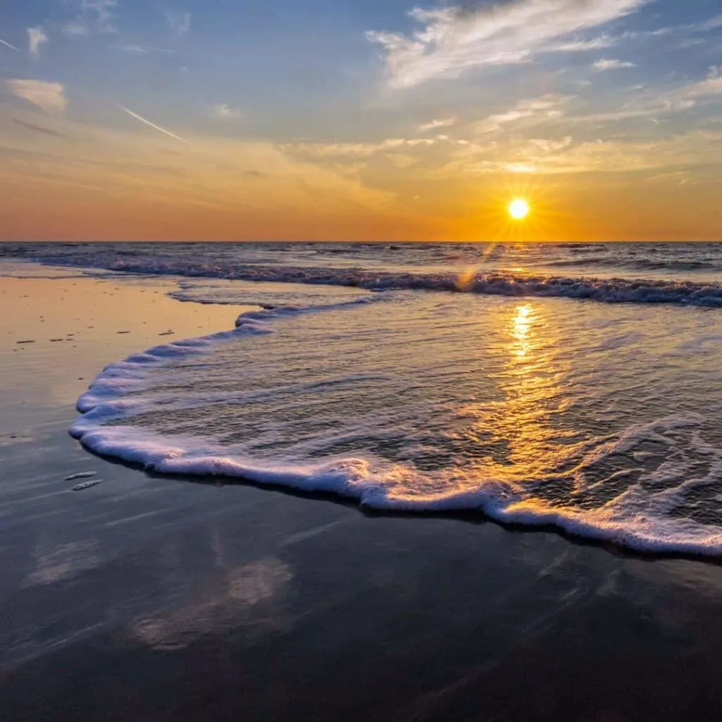 the sun sets over the ocean and waves on a beach