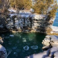 best things to do in Door County in February, View of large pool of frozen water surrounded by trees and tall rock walls covered in ice with a large body of water to one side