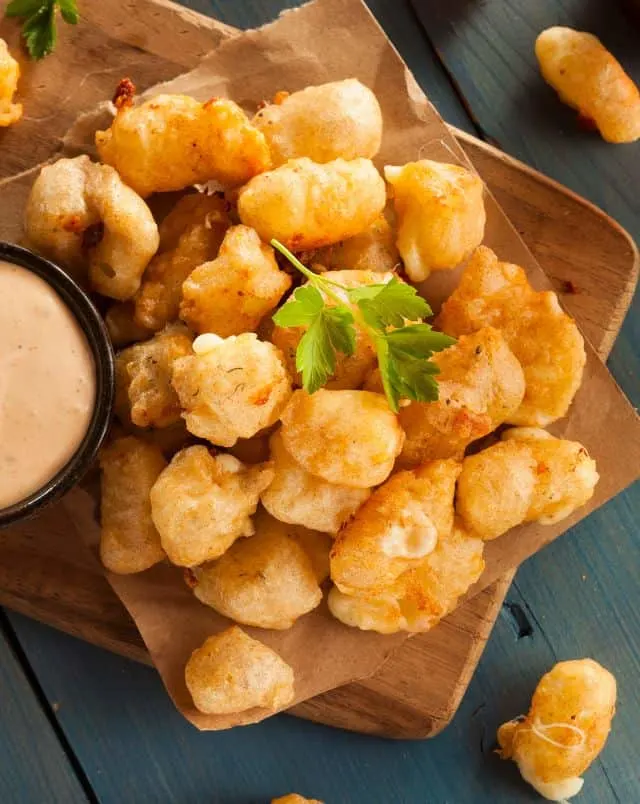 food to enjoy during February in Door County, Close up shot of a delicious pile of deep fried cheese curds on a wooden board with a small dish of dip beside them
