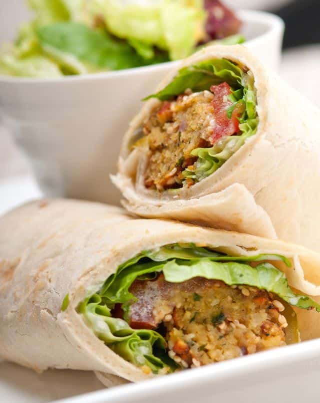 Top cafes in Milwaukee, Close up shot of a plate with two halves of a falafel wrap with a bowl of green salad leaves behind