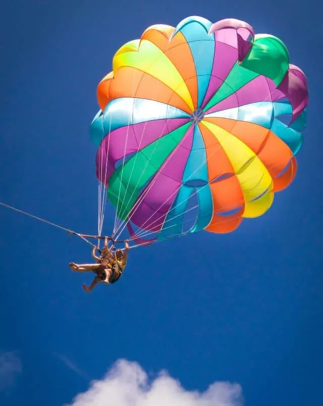 top things to do in Vilamoura Algarve, Two people attached to a large colorful parachute being pulled by a cable through a bright blue sky in the sun