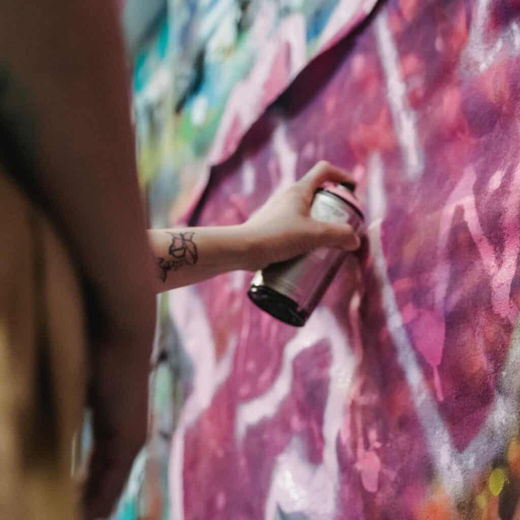 a hand pressing purple spray paint on a wall with art