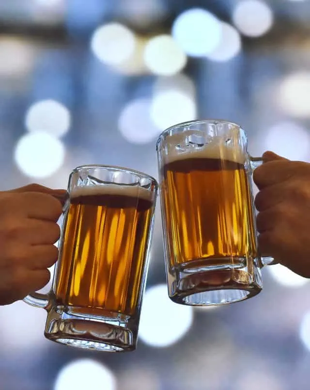 close up of two hands holding beer mugs and about to clink them together
