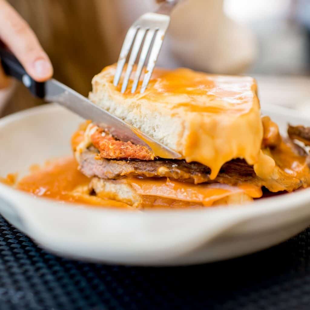 a person eating a Francesinha  sandwich with a fork and knife