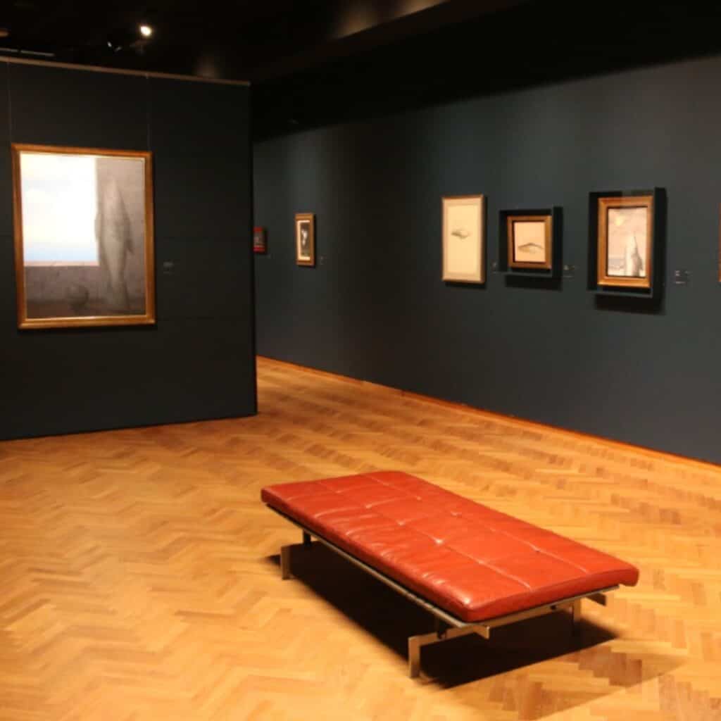inside a museum with paintings hanging on a black wall and an empty bench
