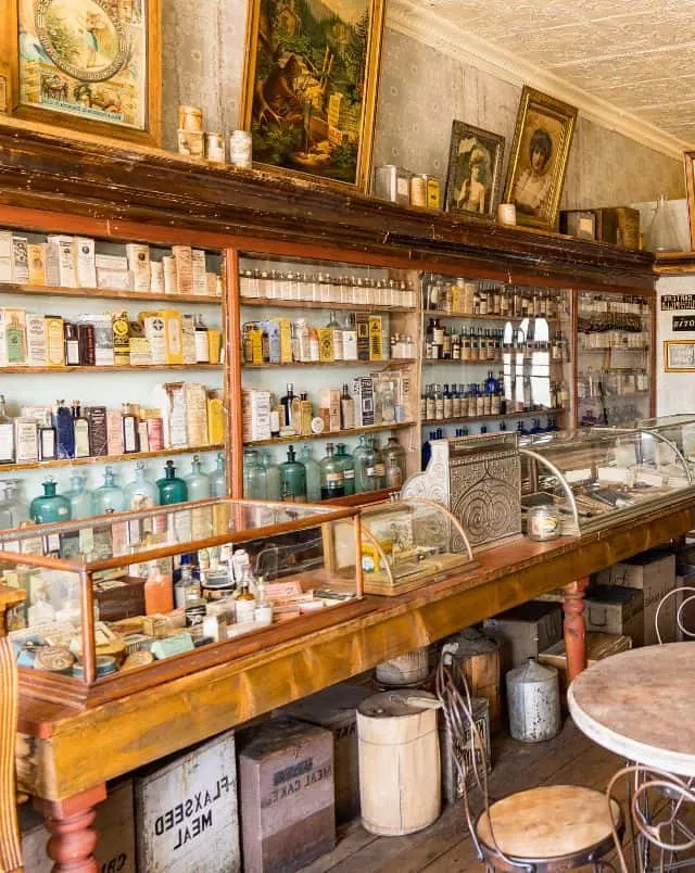 Wisconsin attractions for kids, Interior of a period general store with glass cabinets and shelves packed with commercial items packaged in period style with painted pictures in frames on a shelf above and wooden crates of other products underneath the counter