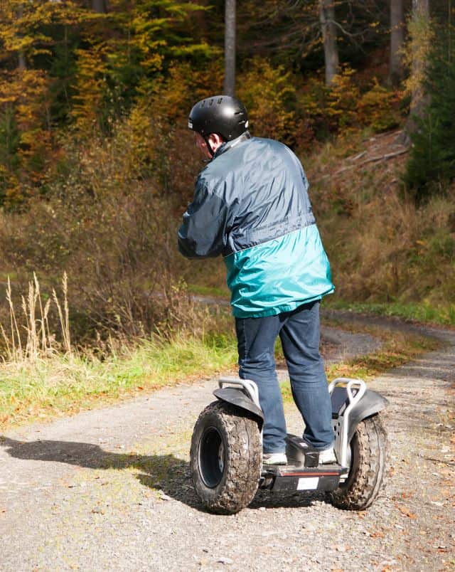Best Monchique tours, Person in a waterproof jacket and black helmet riding a Segway along a gravel track through a forested area in the sunshine