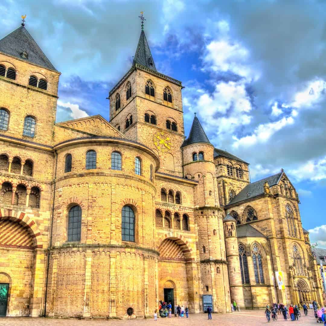 a facade view of a cathedral on a bright day with tourists walking. Where to stay in Belgium