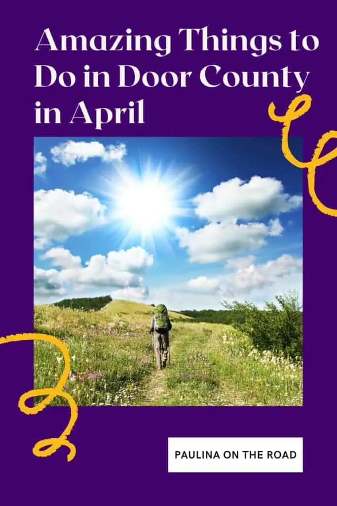 Pin with image of a person wearing a large camping backpack and carrying walking sticks hiking along a trail running through a field of lush green grass and colorful flowers towards rolling hills under a dramatic blue sky with white fluffy clouds and a bright and shining sun, caption reads: Amazing Things to Do in Door County in April from Paulina on the Road