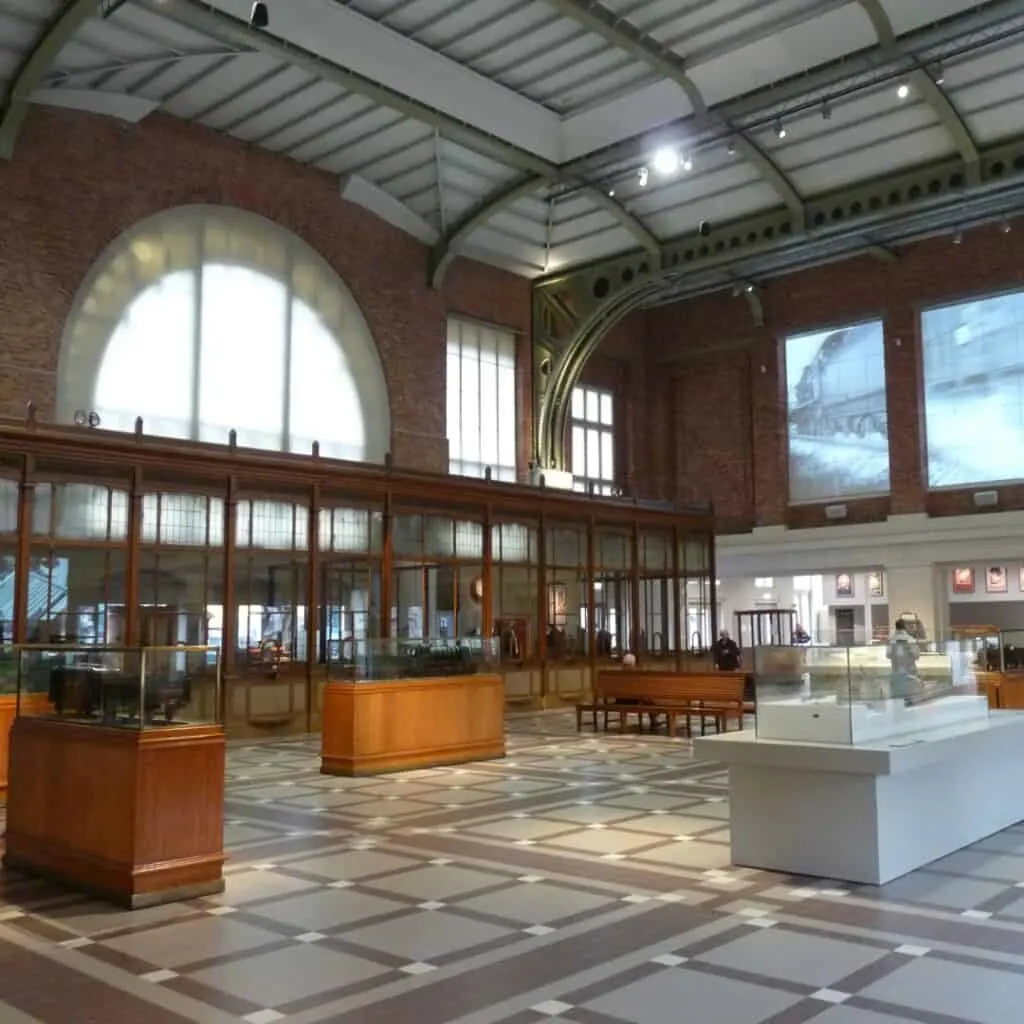 inside a museum with high ceilings and train figures on a glass display