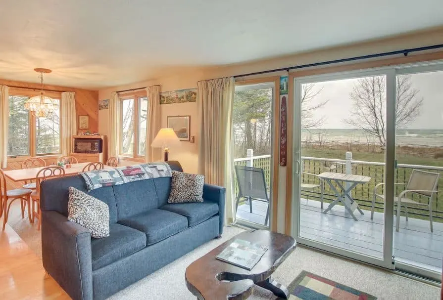 living room area with sofa, dining table, and windows opening to a balcony overlooking the lake at the Serene Lakefront Home in Bailey's Harbor, Wisconsin